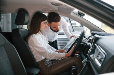 Otomobilde oturuyor. Beyaz elbiseli bir adam araba galerisinde birlikte..