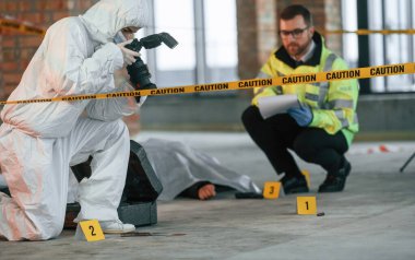 Kadın kamerayla fotoğraf çekiyor. Dedektifler cesedin yanındaki suç mahallinde kanıt topluyorlar..