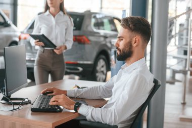 Masada oturup çalışmak. Beyaz elbiseli bir adam araba galerisinde birlikte..