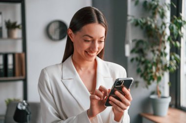 Akıllı telefon kullanıyor. Resmi giyinmiş güzel bir kadın ofiste çalışıyor..