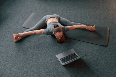 Bilgisayarı kullanarak online dersler almak. Yoga elbiseli genç bir kadın içeride spor yapıyor..