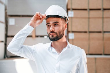 Beyaz kasketli. Depo işçisi depoda bir sürü ürünle birlikte..