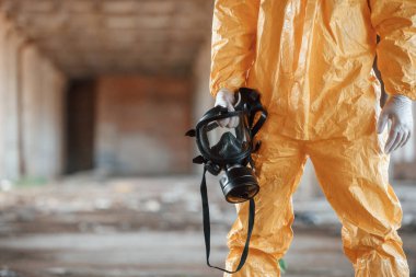 Gaz maskesi tutuyor. Kıyamet sonrası binanın harabelerinde kimyasal koruma kıyafeti giymiş bir adam..