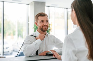 Müşteri asistanı. Beyaz gömlekli adam kadının yardımıyla otelde bir oda istiyor..