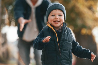 Çocuk gülümsüyor ve koşuyor. Eğleniyorum. Baba ve küçük oğlu gündüz vakti dışarıda beraberler..