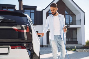 Aracı şarj etme işlemi. Genç şık adam, gündüz vakti elektrikli arabayla geziyor..