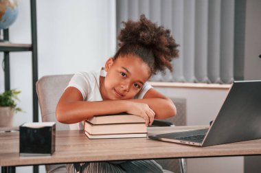 Kitaplar ve dizüstü bilgisayarla. Şirin Afrikalı Amerikalı kız öğrenci masanın yanında oturuyor..