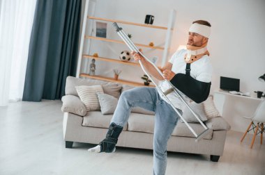 Koltuk değnekleriyle gitar çalıyormuş gibi yapıyor. Evdeki adam içeride. Yaralı..