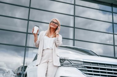 Binanın önünde dikilip içki içiyoruz. Beyaz elbiseli kadın araba galerisinde..