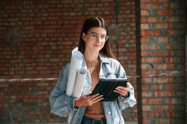 Planı ellerindeyken. Genç bir kadın inşaat alanındaki tamamlanmamış binada duruyor ve bir proje üzerinde çalışıyor..