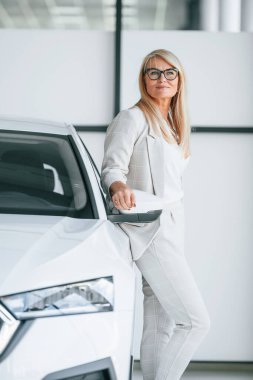 Arabaya yaslanarak. Beyaz elbiseli kadın araba galerisinde..