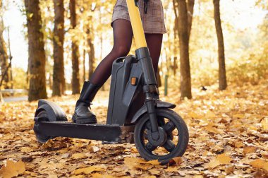 Ormanda sonbahar sezonunda elektrikli scooter kullanan kadınların bacaklarını yakın plan çek..