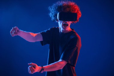 Yarış oyunu. VR gözlüklü. Kıvırcık saçlı genç adam kapalı alanda neon ışıkla aydınlatılır..