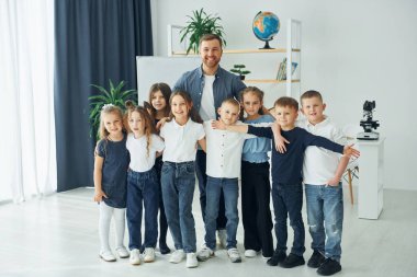 Ayakta ve gülümsüyor. Okulda öğretmenle birlikte bir grup çocuk öğrenci..