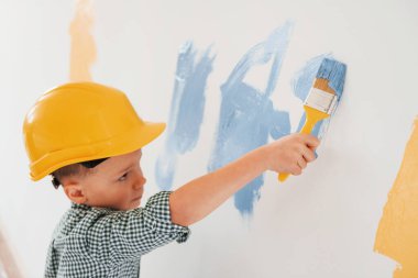 Mavi ve sarı renkler kullanarak. Küçük çocuk ev odasında duvarları boyuyor..