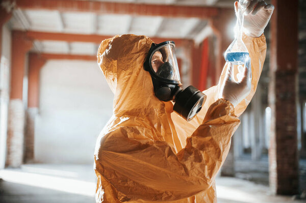 A test tube with radioactive materials. Man dressed in chemical protection suit in the ruins of the post apocalyptic building.