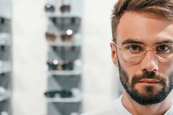 stock image Close up portrait. Stylish man with beard choosing glasses in the optics store.