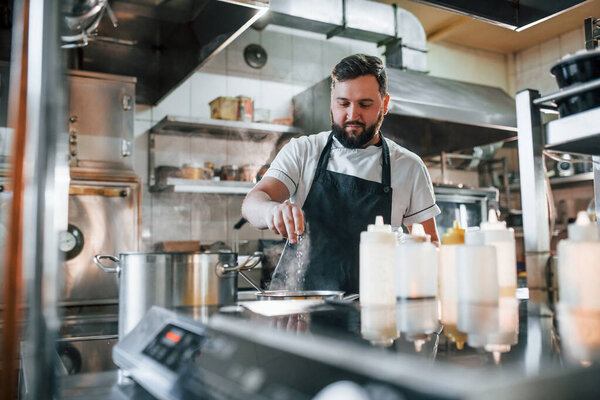 Pouring some salt. Professional chef preparing food in the kitchen.