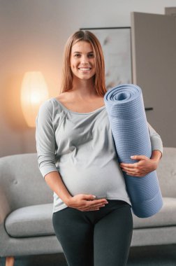 Mavi renkli yoga minderi hazır. Güzel hamile kadın evde..