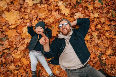 Düşen yapraklarla kaplı yerde yatıyordu. Baba ve küçük oğlu gündüz vakti dışarıda beraberler..