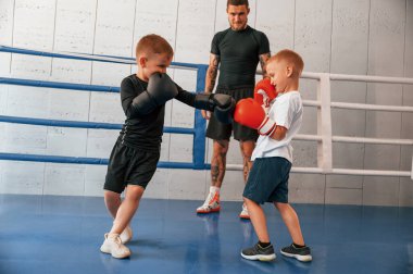 Ringde dövüşmek. Genç dövmeli koç çocuklara boks teknikleri öğretiyor..