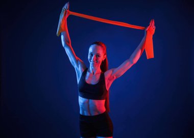 Ellerini uzatmak için sarı renkli bant. Güzel kaslı kadın stüdyoda neon ışıklı..