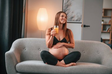 Kanepede oturup portakal suyu içmek. Güzel hamile kadın evde..