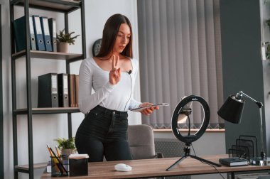 Akıllı telefon kürsüde, kaydediyor. Beyaz elbiseli genç ve güzel bayan ofiste..