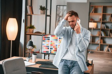 Telefonla konuşuyorum. Genç erkek tasarımcı modern ofiste..