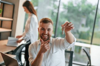 Yeni dairenin anahtarlarını saklıyorum. Erkek ve kadın modern ofiste birlikte çalışıyorlar..