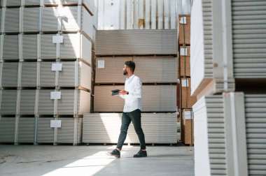Tablet tutuluyor ve verileri kontrol ediliyor. Depo işçisi depoda bir sürü ürünle birlikte..