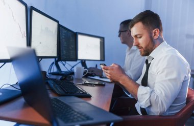 Masada bir sürü ekran var. Ofiste değişim teknolojisiyle çalışan iki borsacı..