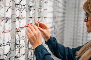 Ürün duvarda asılı. Mağazadaki kadın yeni gözlük deniyor..