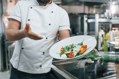 Salatayı tutuyor ve gösteriyor. Profesyonel aşçı mutfakta yemek hazırlıyor..