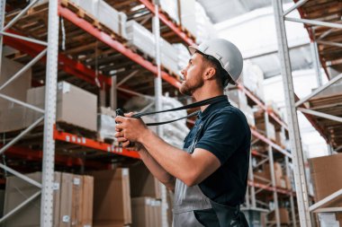 Elinde dijital tabletle. Üniformalı eleman gündüz vakti depoda çalışıyor..