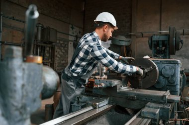 Üniformalı fabrika çalışanı içeride. Metal üzerinde işlem yapılıyor..
