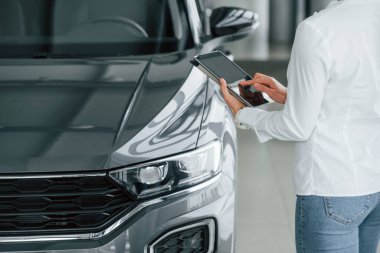 Arabanın yanında duruyor. Kadın gündüz vakti otosalonda..