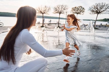 Annesiyle birlikte göl kenarındaki çeşmede eğlenen küçük kız..