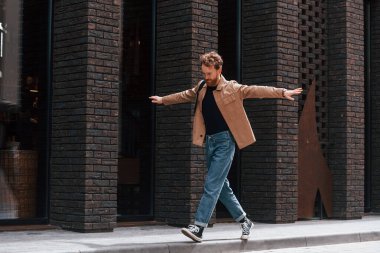 Kaldırımda yürürken eğleniyorum. Sakallı, haki renkli ceketli ve kot pantolonlu şık bir adam binanın yanında..