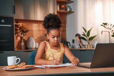 Çizim yapmak için dizüstü bilgisayar ve kağıtla masada oturuyordum. Gündüz vakti evde rahat giyinen sevimli siyah kız var..