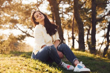 Güzel bir kadın gündüz vakti ormanda çimlerin üzerinde oturuyor..