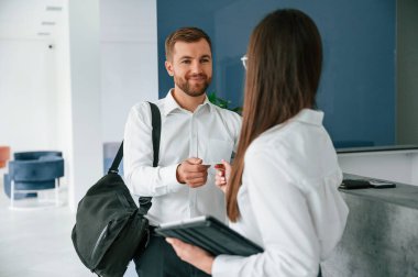 Beyaz gömlekli adam kadının yardımıyla otelde bir oda istiyor..