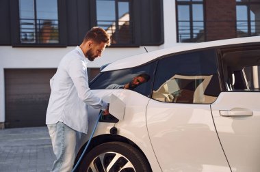 Kabloyu şarj ediyorum. Genç şık adam, gündüz vakti elektrikli arabayla geziyor..