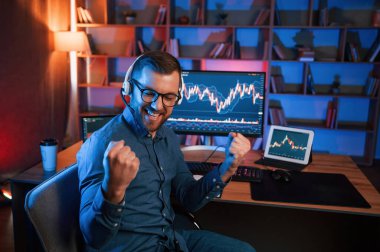 Happy borsa simsarı içeride bilgisayar başında çalışıyor ve başarıyı kutluyor. Değişim ve para kavramı.