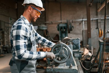 Fabrika makinesiyle çalışmaya odaklanmış. Üniformalı işçi içeride..