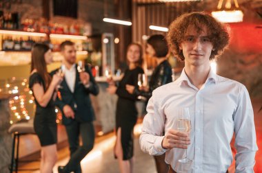 Bir bardak şampanyası olan adam. Güzel giyinmiş bir grup insan içeride yeni yılı kutluyorlar..