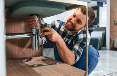 Sifonu tamir etmekle meşgul. Mavi üniformalı tesisatçı banyoda çalışıyor..