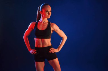 Eller belde, ayakta. Güzel kaslı kadın stüdyoda neon ışıklı..