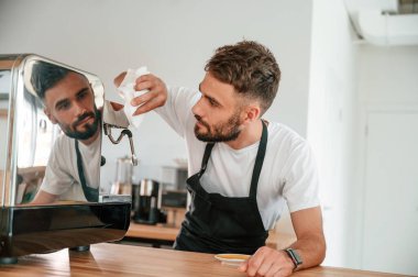 Kahve makinesini temizliyorum. Beyaz gömlekli ve siyah önlüklü kafe çalışanı içeride..