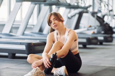 Yerde dinleniyor. Spor elbiseli genç bir kadın spor salonunda spor yapıyor..